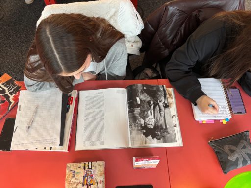 Zwei Personen sitzen an einem Tisch, lesen Bücher und machen Notizen.