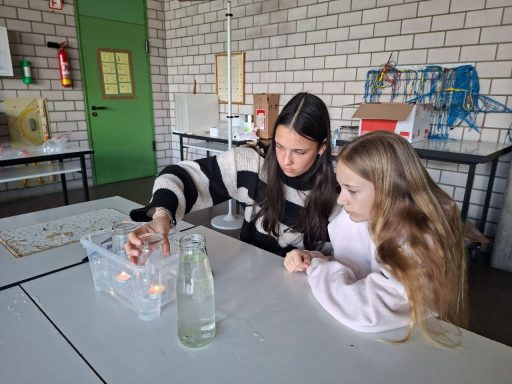 Zwei Mädchen experimentieren mit Wasser und Behältern in einem Klassenzimmer.