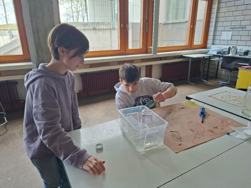 Zwei Kinder experimentieren mit einer Wasserbehälter auf einem Tisch.