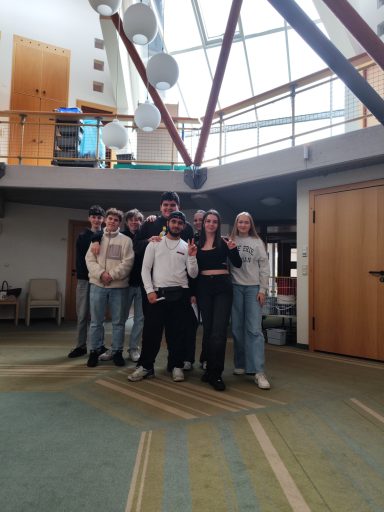 Sechs Personen stehen in einem modernen Innenraum, lächelnd und in lässiger Kleidung.