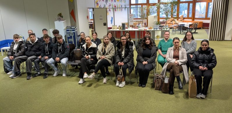 Schüler-meets-Azubi Gruppe von Personen in einem Raum, sitzend in Reihen, mit verschiedenen Ausdrücken.