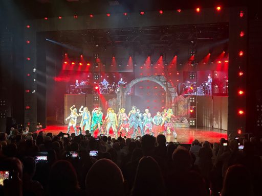 Bunt gekleidete Tänzer auf einer Bühne mit rotem Licht während einer Aufführung.