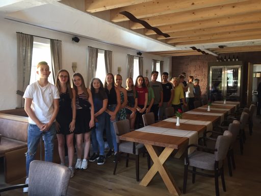 Eine Gruppe junger Menschen steht in einem Restaurant mit Holztisch und Stühlen.