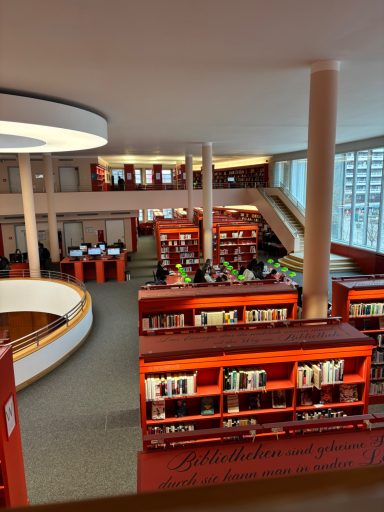 Moderne Bibliothek mit Regalen, Computern und Leseplätzen auf mehreren Ebenen.