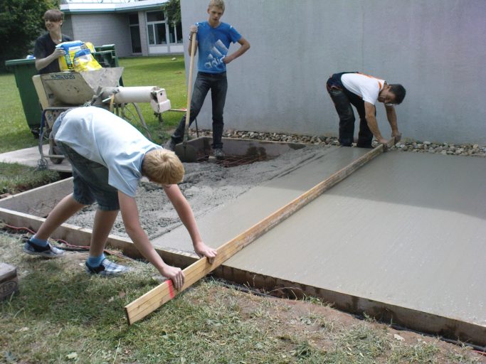 Jugendliche arbeiten gemeinsam an der Betonierung eines Fußweges.