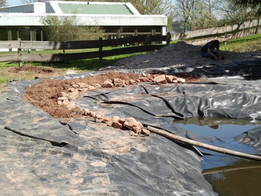 Ein Gewässer mit unebenen Ufern, umgeben von Erde und provisorischem Materialien.