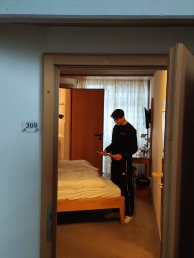 Mann steht in einer Hotelzimmer-Türe und schaut auf sein Handy.