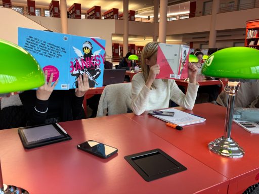 Drei Personen in einer Bibliothek halten Plakate vor ihren Gesichtern. Grüne Tischlampen vorhanden.