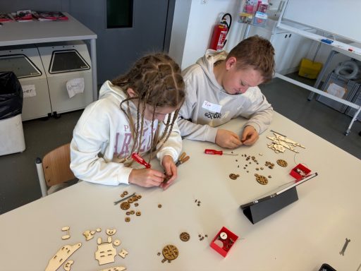 Kinder basteln mit Holzmaterialien und Werkzeugen in einem Klassenzimmer.