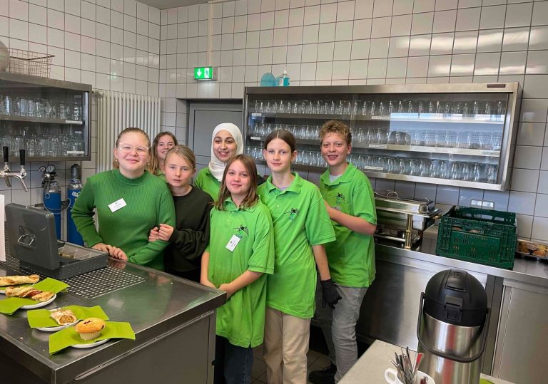Gruppe von sieben Personen in grünen T-Shirts in einer Küche, lächelnd und arbeitend.