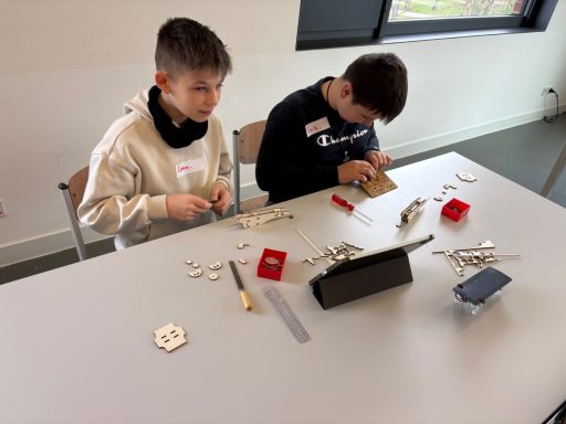 Zwei Jungen arbeiten an einem Tisch mit Bastelmaterialien und einem Tablet.