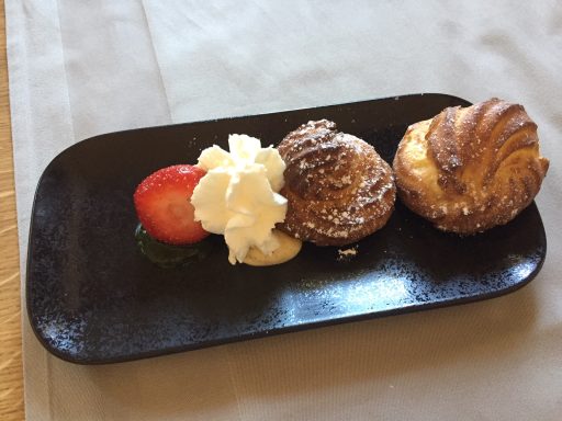 Drei Gebäckstücke mit Sahne und Erdbeere auf einem schwarzen Teller.